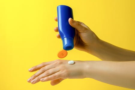 Female hands hold sunscreen on yellow background