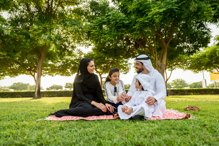 Happy middle-eastern family having fun in a park in Dubai - Parents and kids celebrating the weekend in the nature