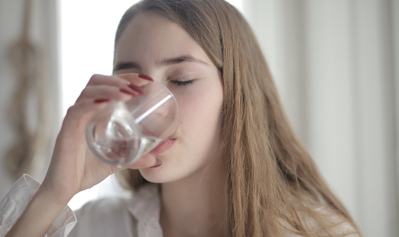 Woman in White Shirt Drinking Water from Clear Glass with Her Eyes Closed. Drinking water to ease dry mouth