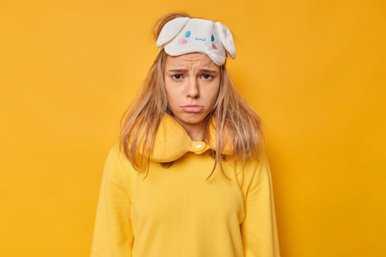 Woman sad to wake up early in morning wears sleepmask on forehead neck pillow casual jumper needs more rest isolated on yellow. people napping and sleeping concept. Sleep disorder concept.