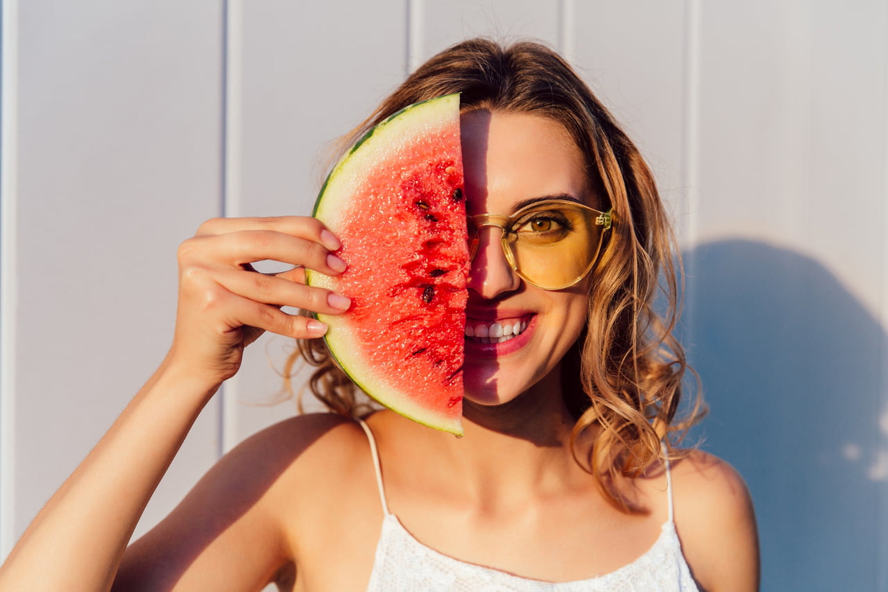 Funny woman in sunglasses hiding a half of her face with piece of watermelon. Happy and healthy summer concept.