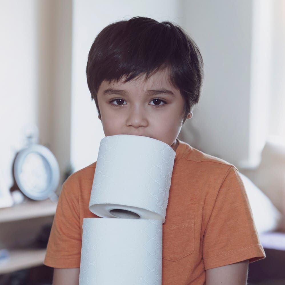 Child carrying a stack of toilet paper with blurry living room background, kid holding toilet roll, Young boy suffers from diarrhea holding toilet paper, Children health care Diarrhea in children concept