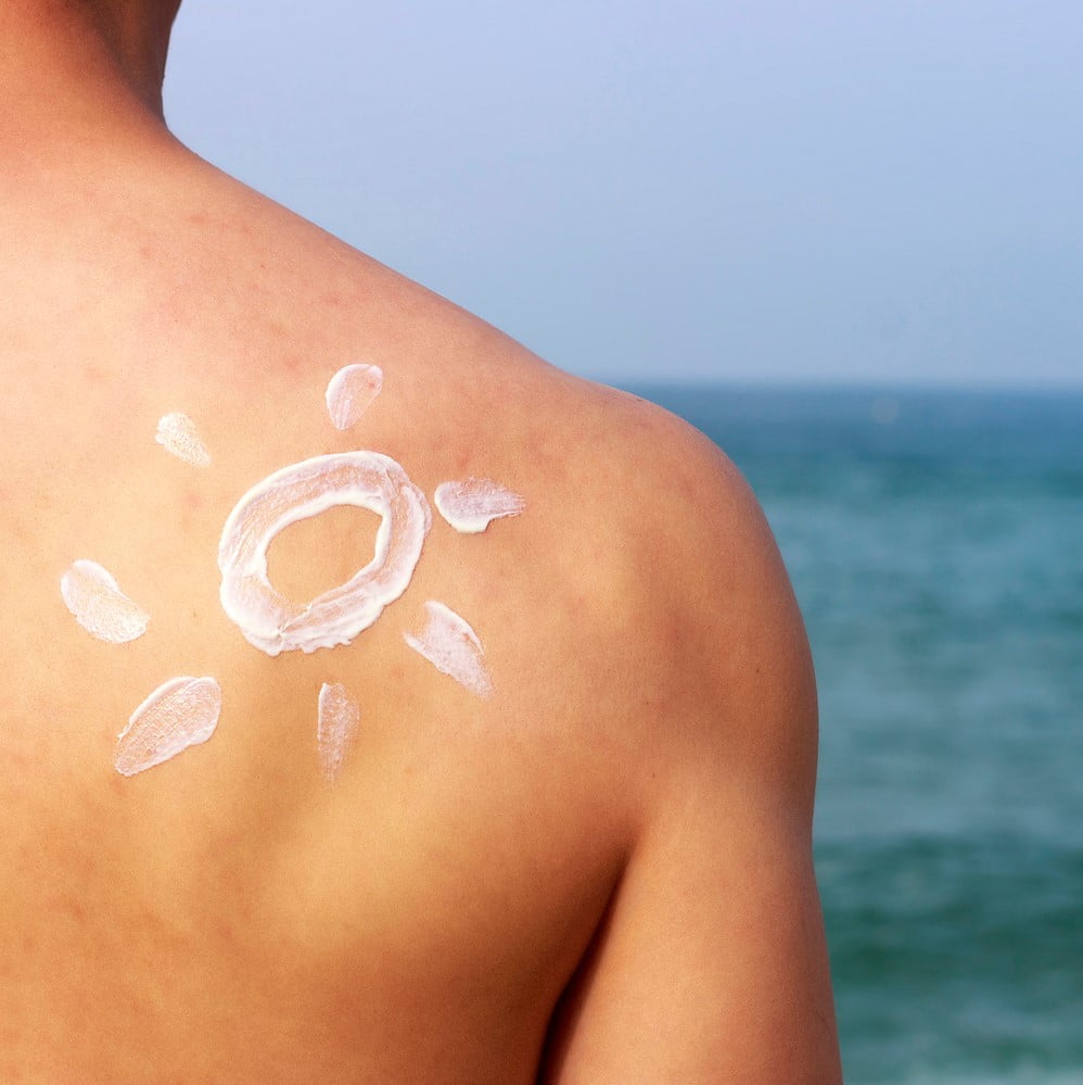 Sunscreen on a man's back against the sea, a skin protection concept. Artificial tanning concept. Dangers of Artificial Tanning