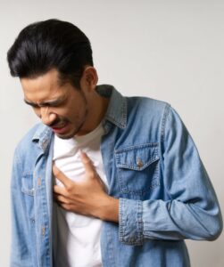 Young Asian man touching his chest where he feels pain due to heart attack problem. His expression on face show how much he hurt. Heart attack is a serious medical emergency. Sickness concept. Heart attack, Acid reflux, Gerd