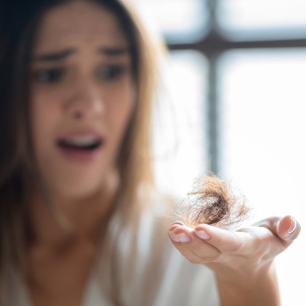 Closeup Of Stressed Young Woman Holding Bunch Of Fallen Hair In Hand, Shocked Millennial Female Standing In Bathroom, Suffering Health Problems Or Alopecia After Chemotherapy, Selective Focus. Can Stress Cause Hair Loss concept.