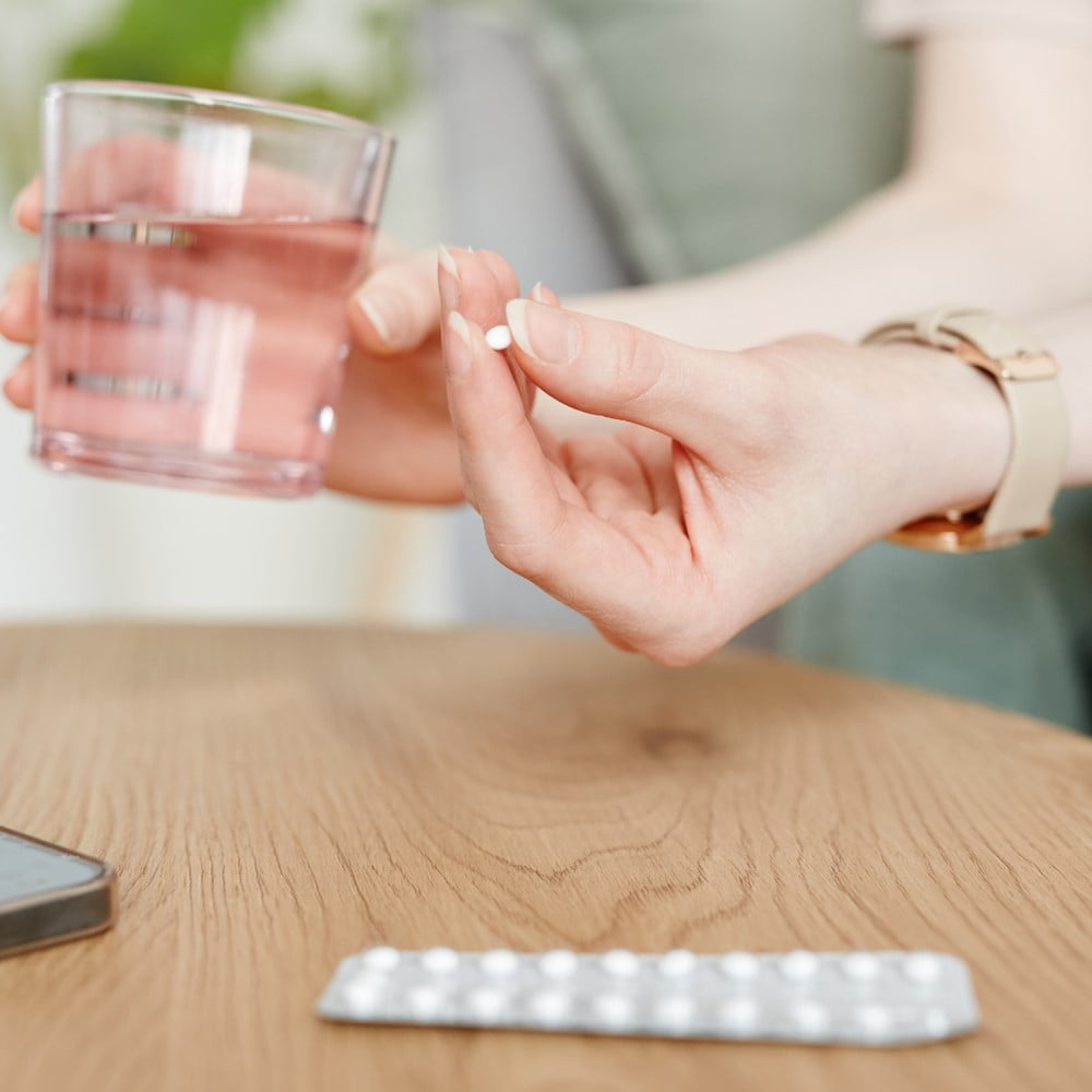 Side view closeup of young woman taking birth control pills with glass of water. Does Birth Control Make You Gain Weight?