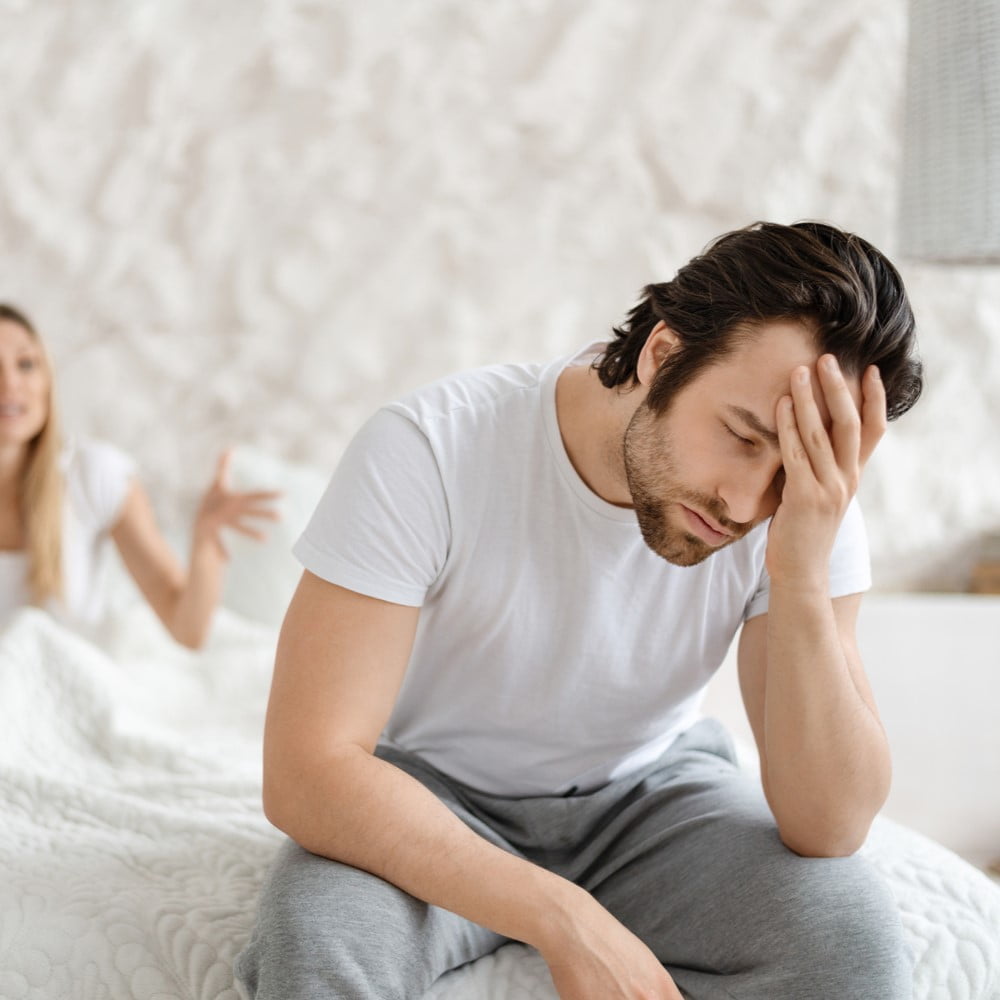 Angry woman shouting at her husband, having conflict while sitting on bed at home, focus on upset man. Married couple having marital crisis, sexual problems, going through breakup or divorce. how erectile dysfunction occurs