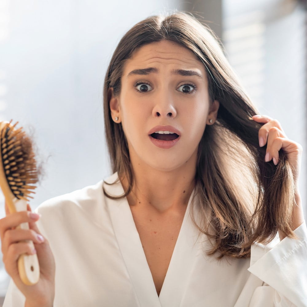 Shocked Young Woman Worried About Hair loss After Brushing Hair in Bathroom, Upset Female Holding Comb Full of Fallen Hair and Looking at Camera with Despair, Emotionally Reacting to Health Problems. Why does hair loss happen? concept