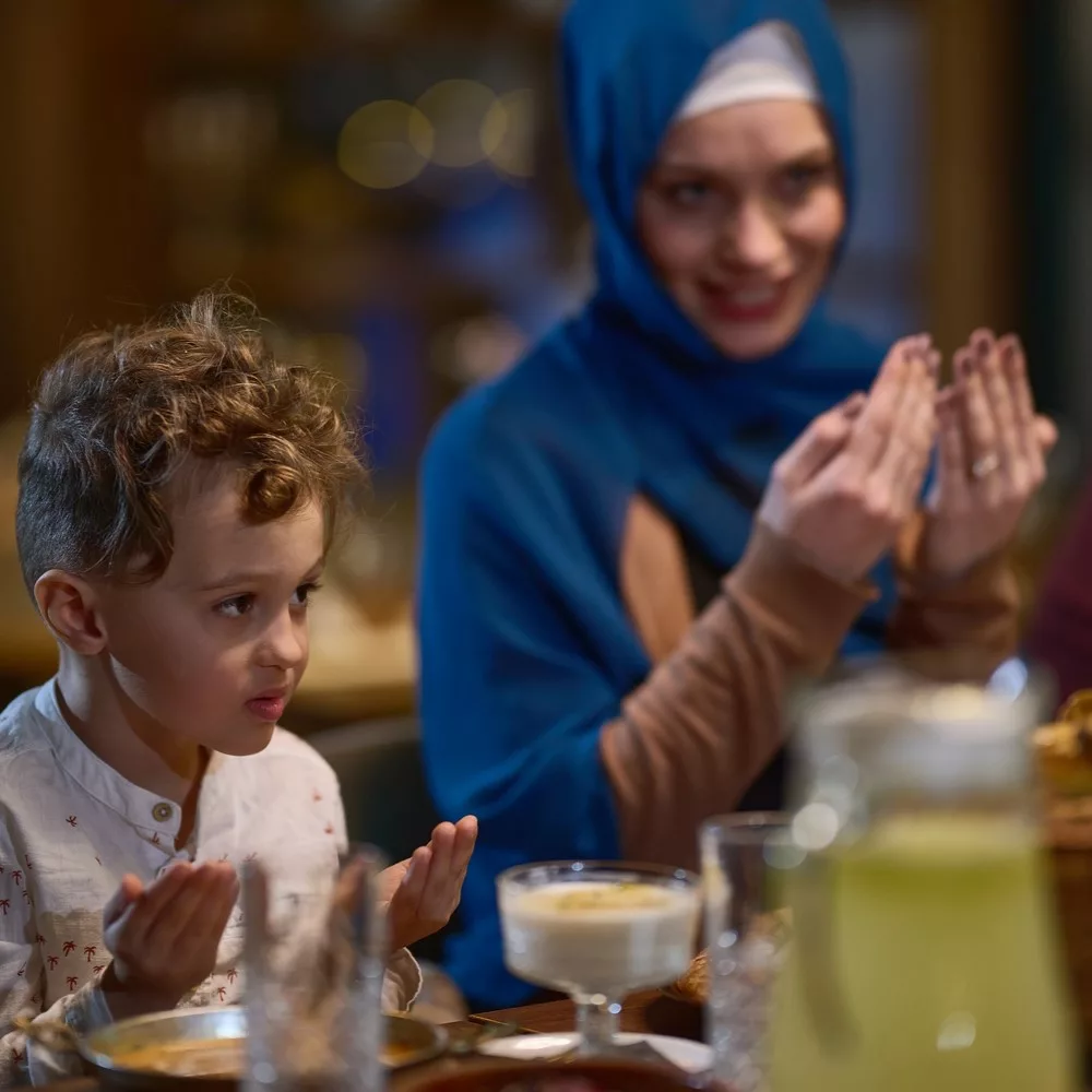 In a modern restaurant setting, a European Islamic family comes together for iftar during Ramadan, engaging in prayer before the meal, uniting tradition and contemporary practices in a celebration of faith and family. Manage Dehydration during Ramadan concept.