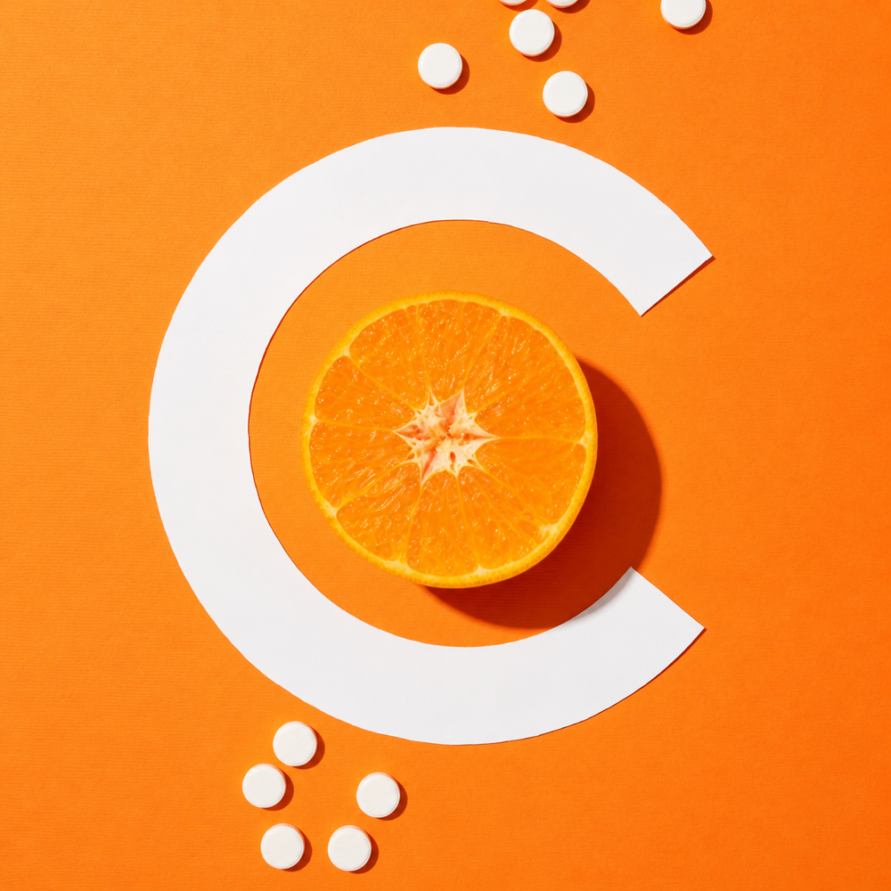 Half an orange sits nestled within a letter C shape, surrounded by scattered white pills, all on a bright orange background. The geometric composition and close-up perspective highlight the texture of the orange slice, with its juicy segments and vibrant color. The arrangement conveys themes of health, wellness, and the benefits of Vitamin C. This image would be ideal for illustrating articles about nutrition, supplements, or healthy eating. It could also be used in advertising campaigns for vitamins or health-related products.